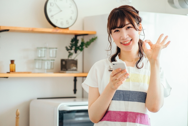 キッチンでスマホを持つ女性（笑顔）